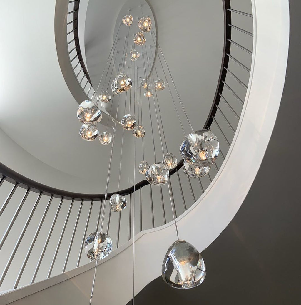 Looking up a white spiral staircase, a Clérachic glass pendant cluster hangs through the well, its clear heads in varied sizes.