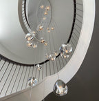 Looking up a white spiral staircase, a Clérachic glass pendant cluster hangs through the well, its clear heads in varied sizes.