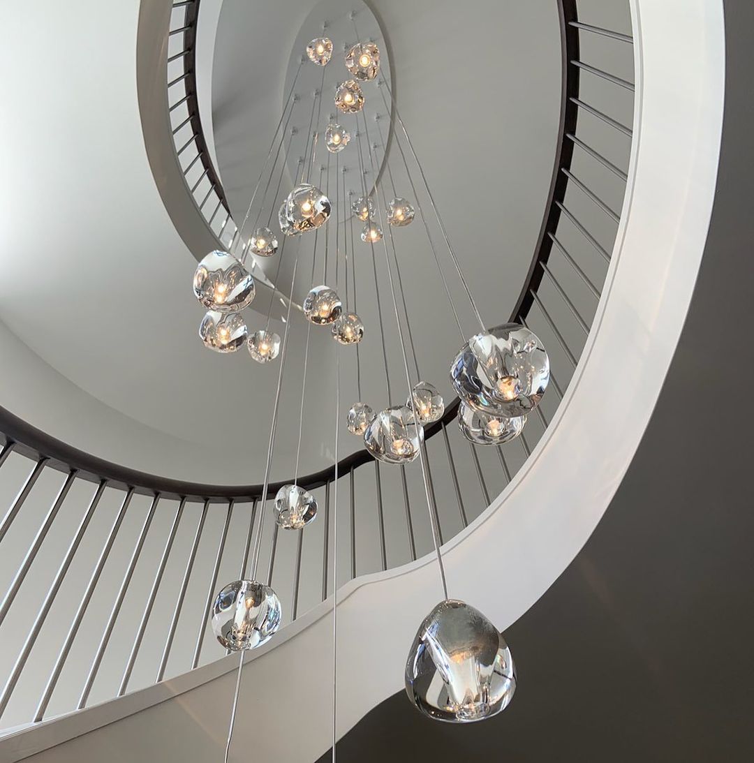 Looking up a white spiral staircase, a Clérachic glass pendant cluster hangs through the well, its clear heads in varied sizes.