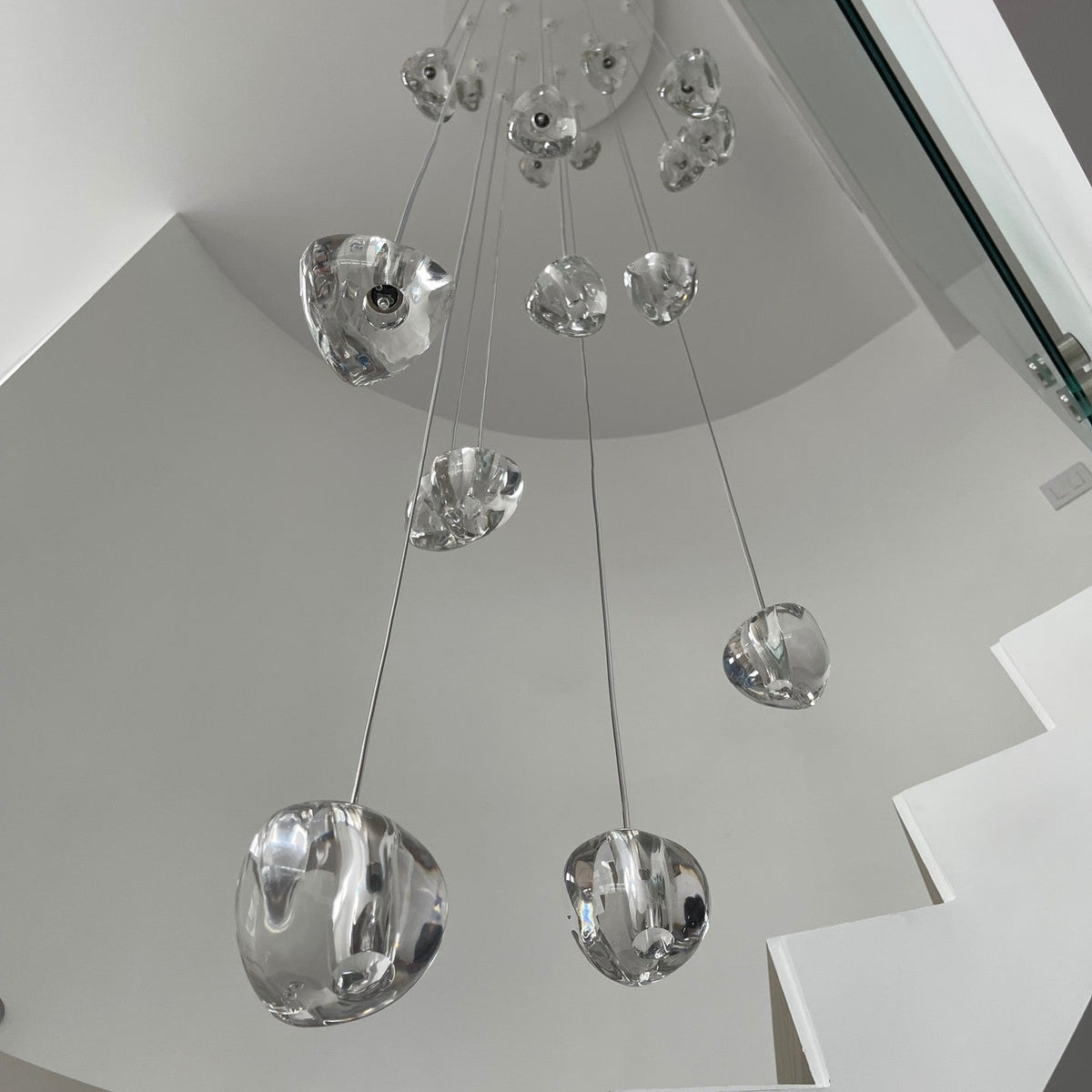 Looking up from below, this Clérachic pendant shows large clear glass heads on long wires dropping through a white stairwell.