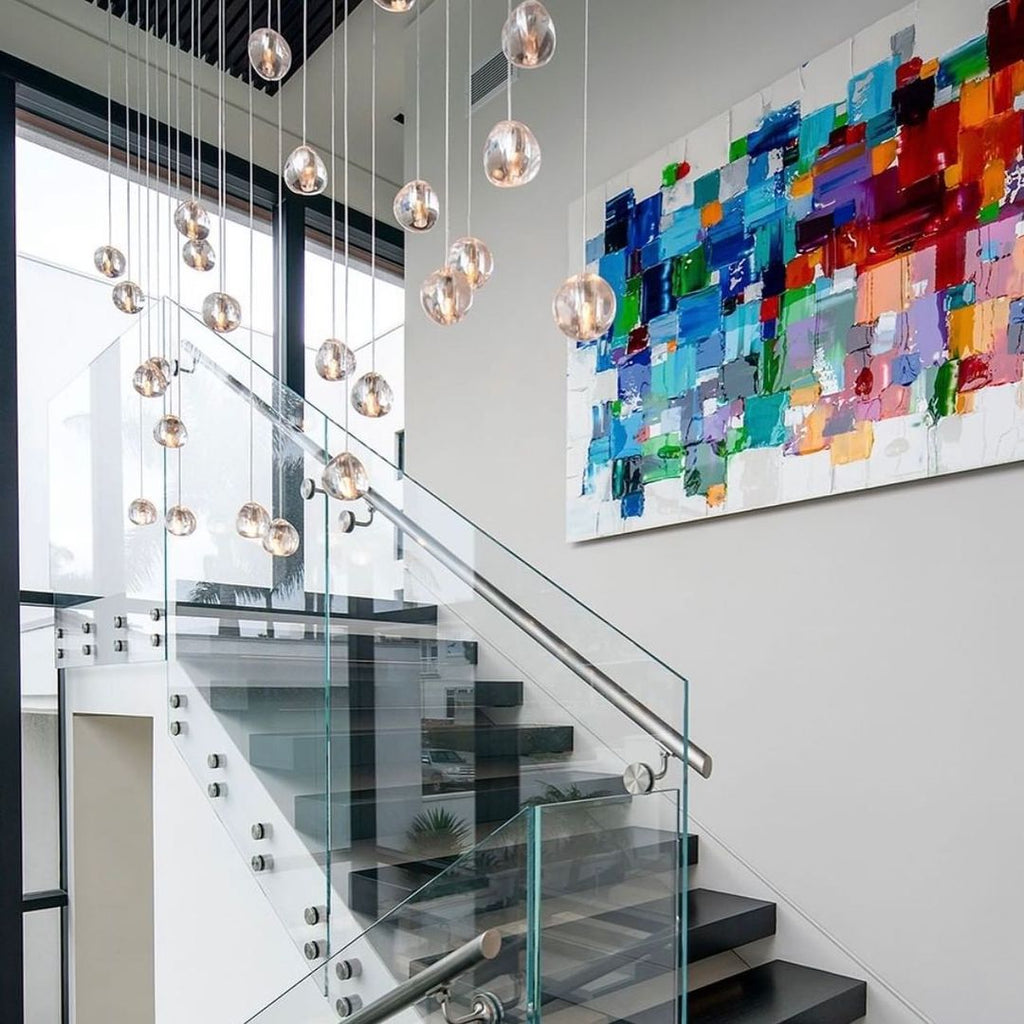 Clear glass heads from this Clérachic pendant drift down beside a glass-sided staircase and a large colourful abstract painting.