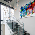 Clear glass heads from this Clérachic pendant drift down beside a glass-sided staircase and a large colourful abstract painting.