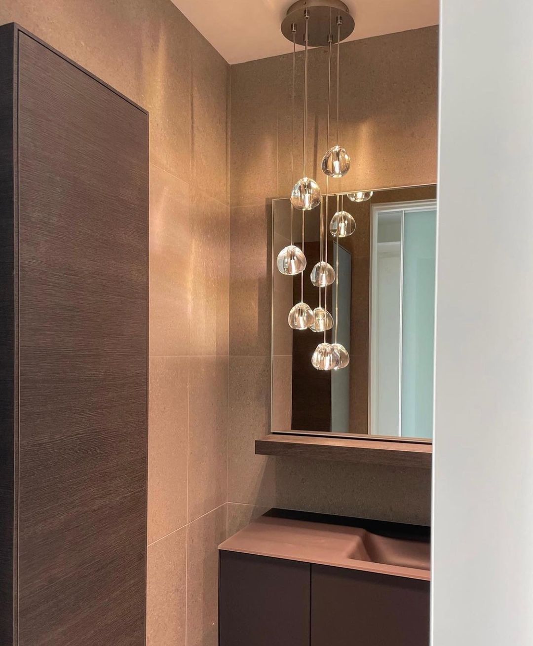 In a small bathroom with a mirror and a vanity, a Clérachic pendant cluster of clear heads hangs from a round canopy.