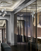 Clear glass heads of this Clérachic pendant hang in a dressing room with mirrored doors, beside a dark green bench.