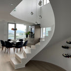 A few clear glass heads of this Clérachic pendant hang beside a white spiral stair, above a round dining table with black chairs.
