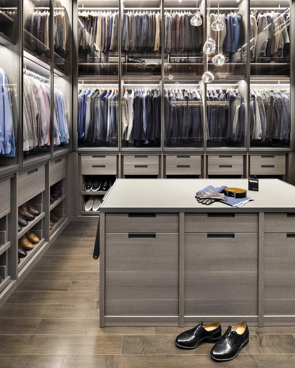 Clear glass heads of this Clérachic pendant hang in a walk-in wardrobe with glass-fronted shelves and a central island.