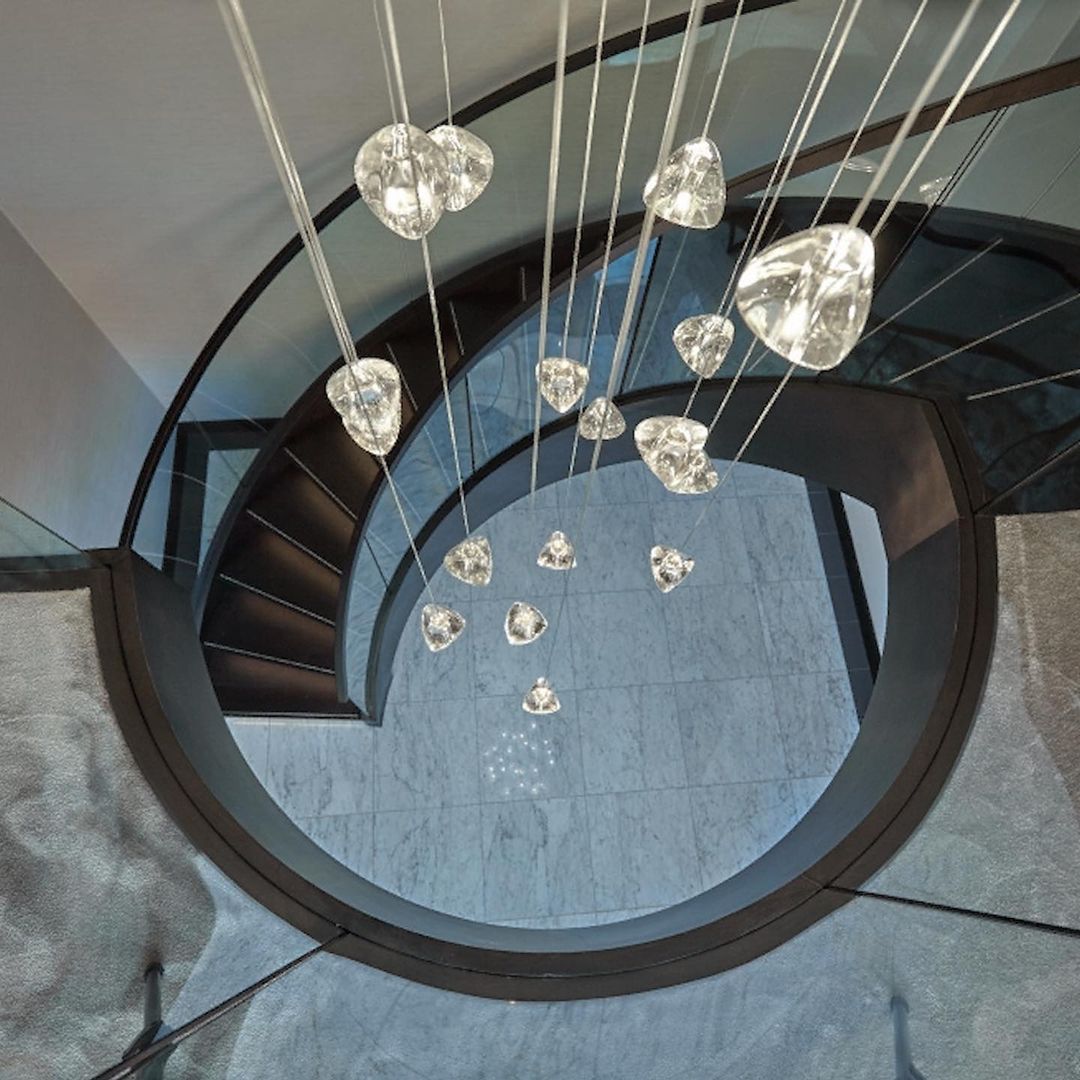 Looking down a spiral stair with a black balustrade, this Clérachic pendant's clear glass heads dangle on long wires.