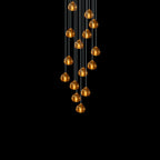 A tapering cluster of amber glass heads from this Clérachic pendant glows against a pure black background.