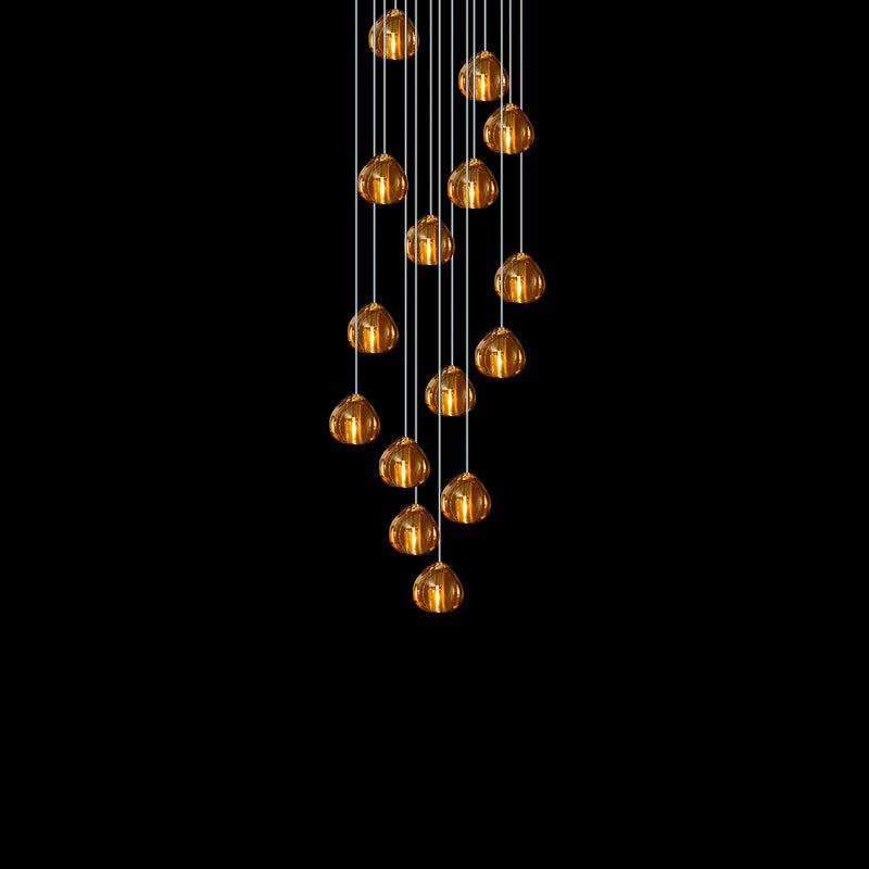 A tapering cluster of amber glass heads from this Clérachic pendant glows against a pure black background.