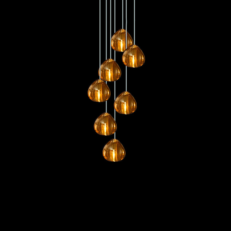Seven amber glass heads of this Clérachic pendant hang in a tight cluster on cords against a black background.
