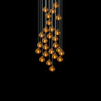 A large group of amber glass heads on this Clérachic pendant hangs on long cords, shown against a black background.