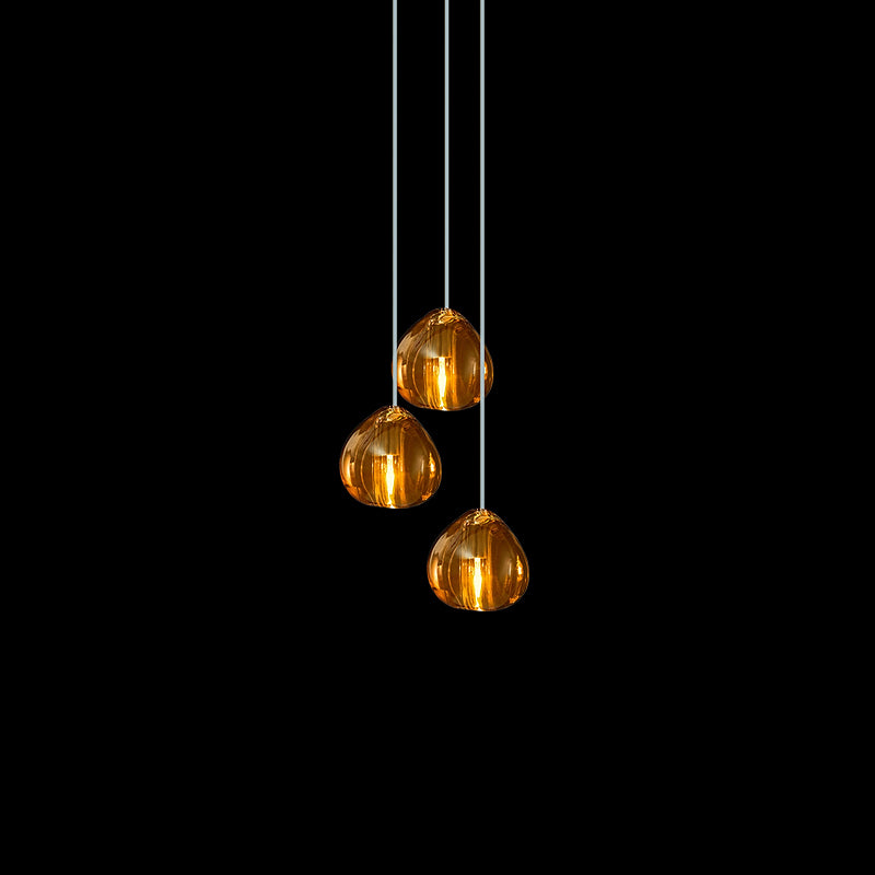 Three amber glass heads from this Clérachic pendant hang at staggered heights on pale cords against black.