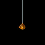 A single amber glass head on this Clérachic pendant hangs on a pale cord against a black backdrop.