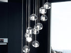 A group of clear glass heads from this Clérachic pendant hangs in a dark kitchen in front of a window with a sea view.