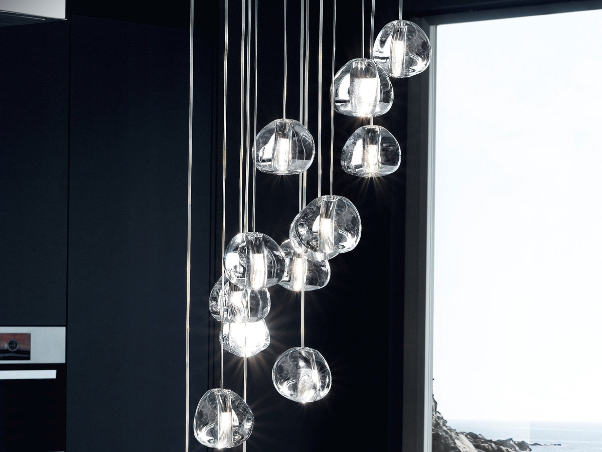 A group of clear glass heads from this Clérachic pendant hangs in a dark kitchen in front of a window with a sea view.