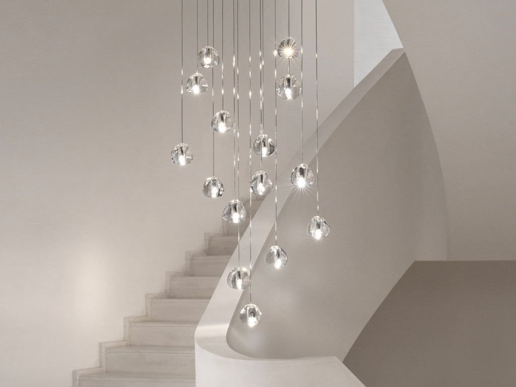 Clear glass heads of this Clérachic pendant follow the curve of a pale staircase, each one lit and hung at a different height.