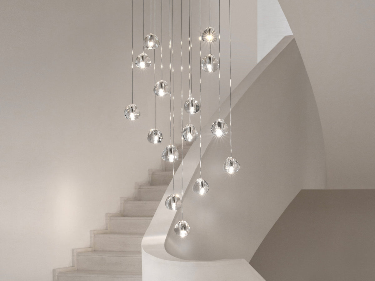 Clear glass heads of this Clérachic pendant follow the curve of a pale staircase, each one lit and hung at a different height.