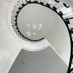 Seen from the floor, this Clérachic pendant cluster floats high in a spiral stairwell ringed with black ironwork and white plaster.