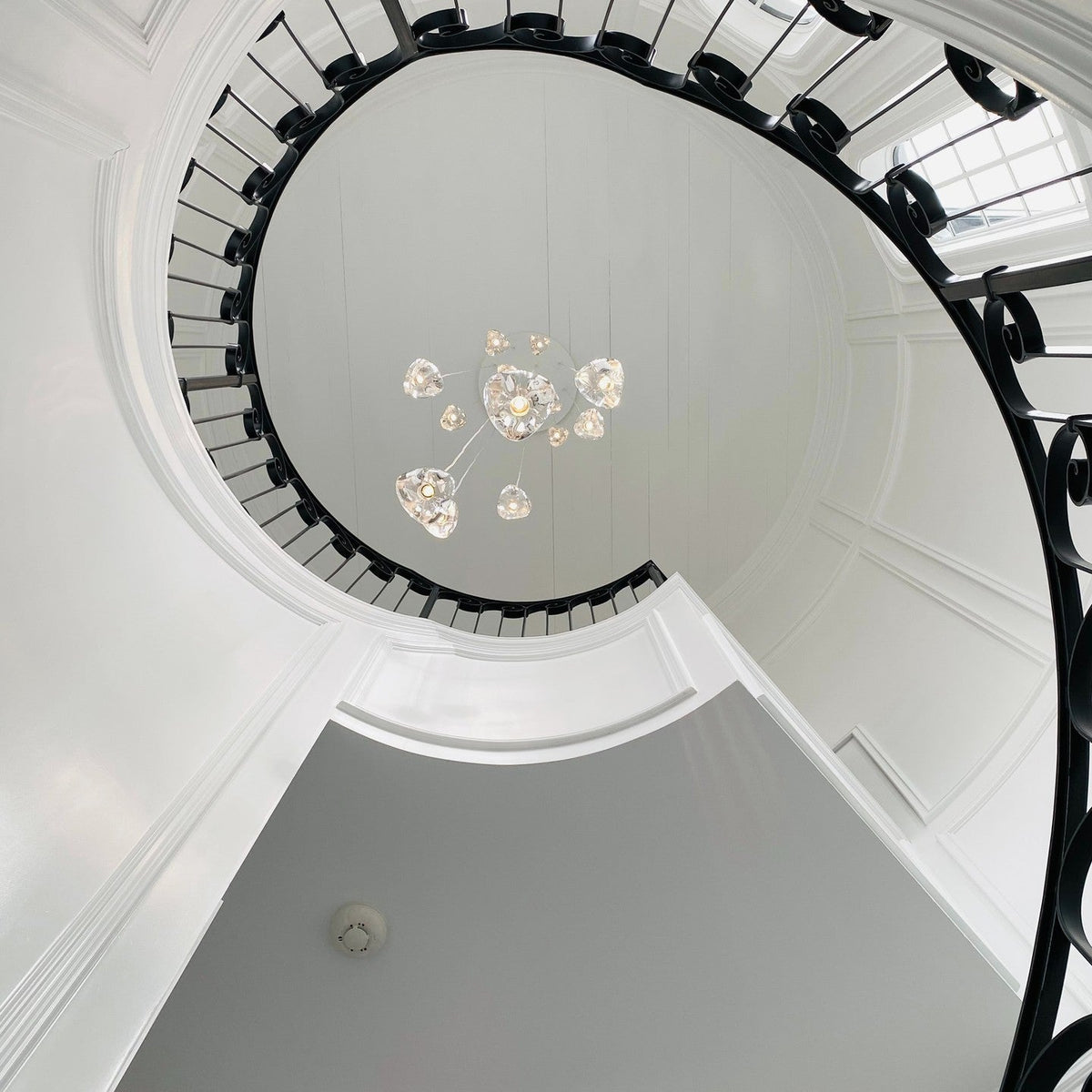 Seen from the floor, this Clérachic pendant cluster floats high in a spiral stairwell ringed with black ironwork and white plaster.
