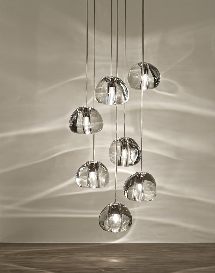 Seven clear glass heads of this Clérachic pendant hang at staggered heights, with light ripples across a soft grey-beige wall.