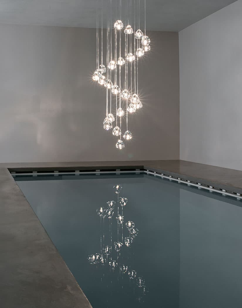Clear glass heads on this Clérachic pendant spiral down in an S shape above an indoor pool, mirrored in the water below.