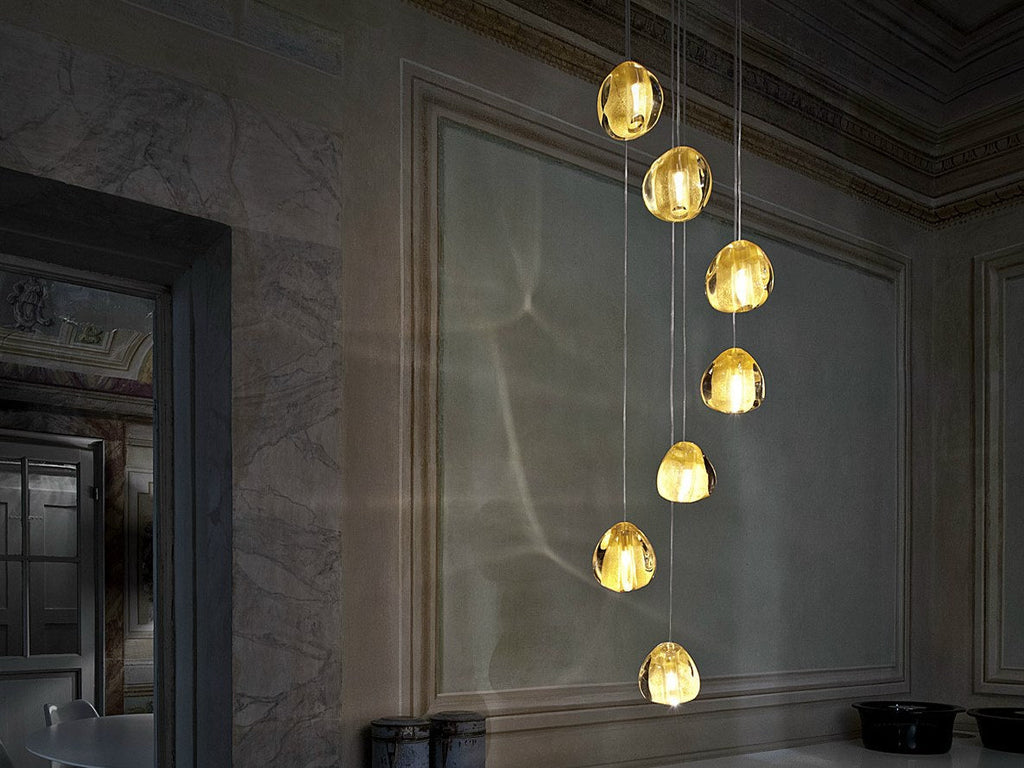 Seven warm yellow-gold glass heads of this Clérachic pendant hang down a panelled stone wall in a dim, formal room.