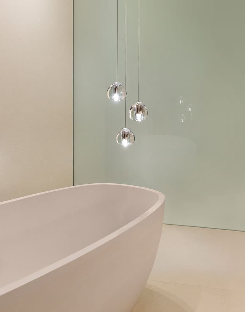 Three clear glass heads of this Clérachic pendant hang over a pale freestanding bath against a soft green wall.