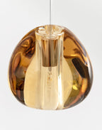 Close view of one amber glass head on this Clérachic pendant, with a brass-coloured lamp holder visible inside, on a white backdrop.