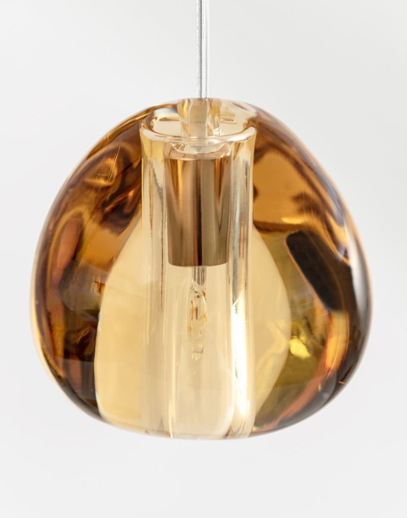 Close view of one amber glass head on this Clérachic pendant, with a brass-coloured lamp holder visible inside, on a white backdrop.