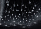Looking up at a dark ceiling, clear glass heads of this Clérachic pendant hang on hundreds of thin wires with streaks of light across the glass.