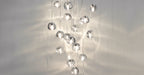 A wide crop of this Clérachic pendant cluster, with clear glass heads sparkling and casting soft reflections on a pale wall.