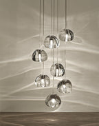 Seven clear glass heads of this Clérachic pendant hang above a wooden floor, with light patterns spread over a pale wall.