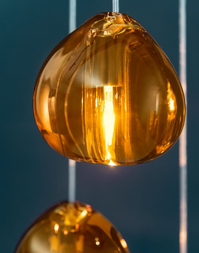 Tight view of an amber glass head on this Clérachic pendant, with a second head below, shown against a dark teal backdrop.