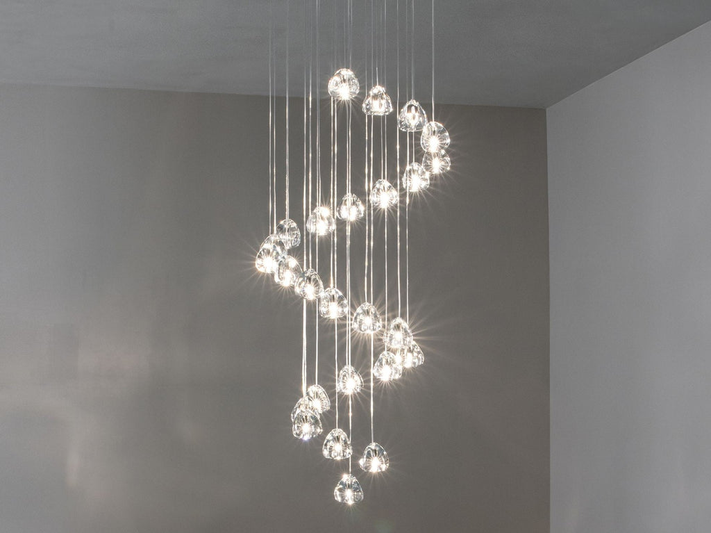 A spiral of clear glass heads hangs down from a high ceiling in a grey room, with this Clérachic pendant seen straight on.