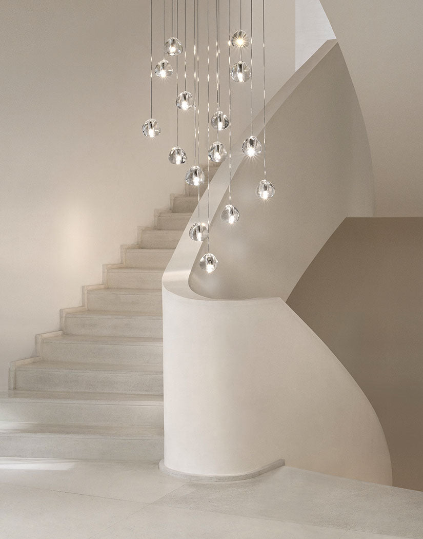 A Clérachic pendant cluster of clear glass heads hangs beside a white stair that curves up and out of sight.