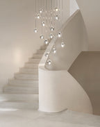 A Clérachic pendant cluster of clear glass heads hangs beside a white stair that curves up and out of sight.