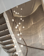 Looking down a spiral timber stair, this Clérachic pendant's clear heads glow in rows against a warm, rippled wall.