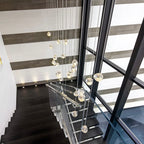This Clérachic pendant's clear glass heads hang down a stairwell with dark treads, a glass balustrade and tall black window frames.