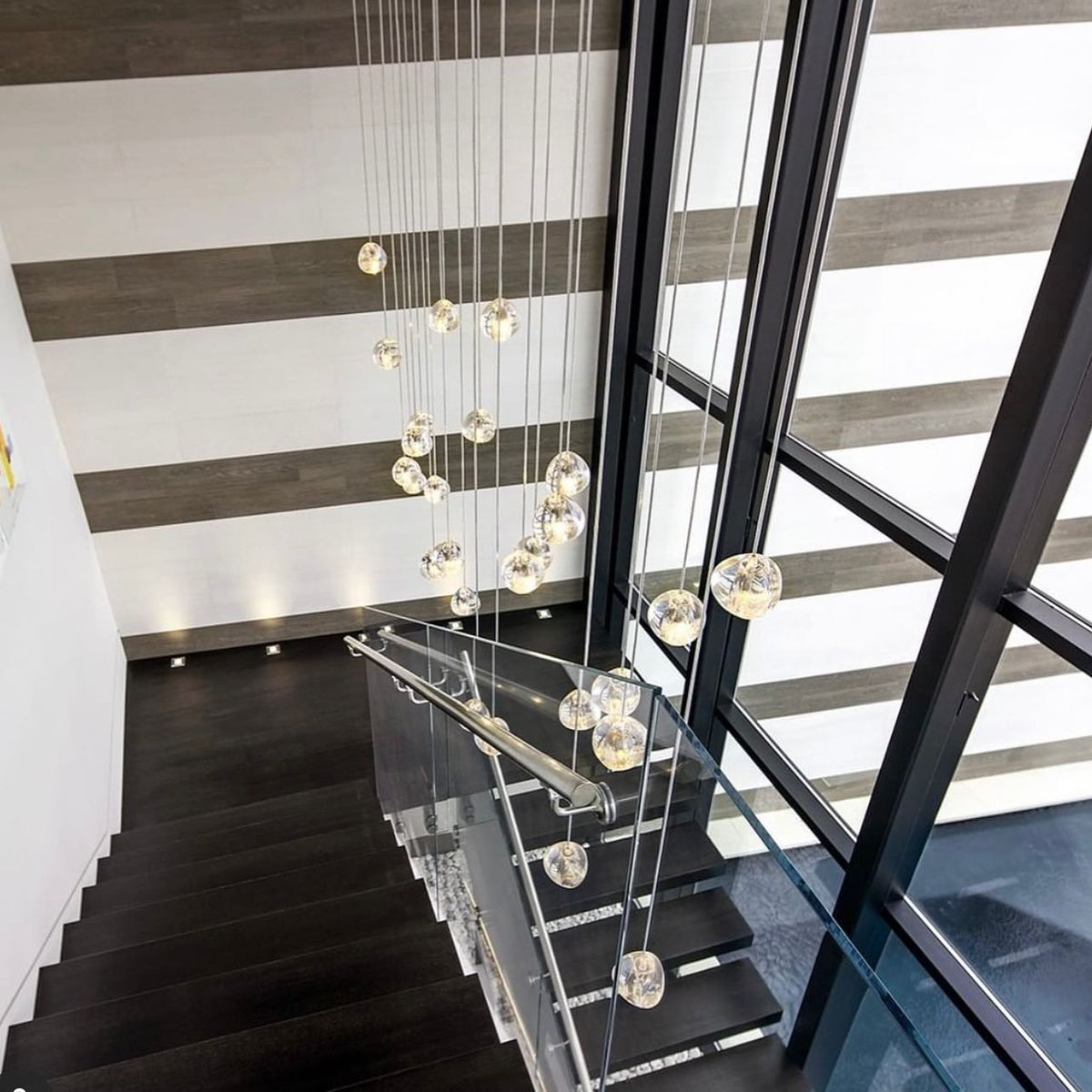 This Clérachic pendant's clear glass heads hang down a stairwell with dark treads, a glass balustrade and tall black window frames.