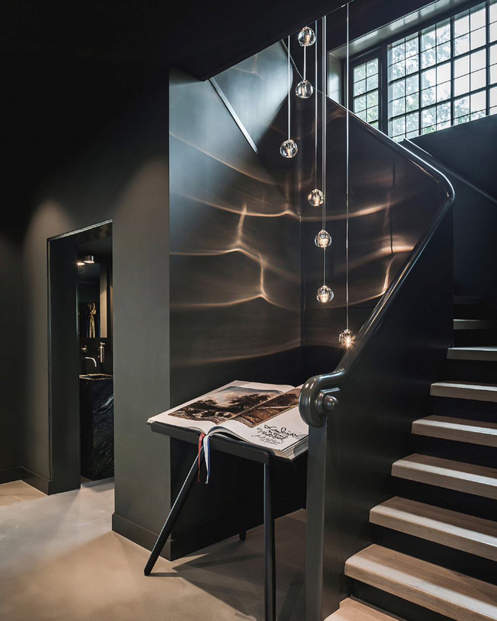 In a dark stairwell with black walls, this Clérachic pendant hangs down the well beside an open book on a stand.