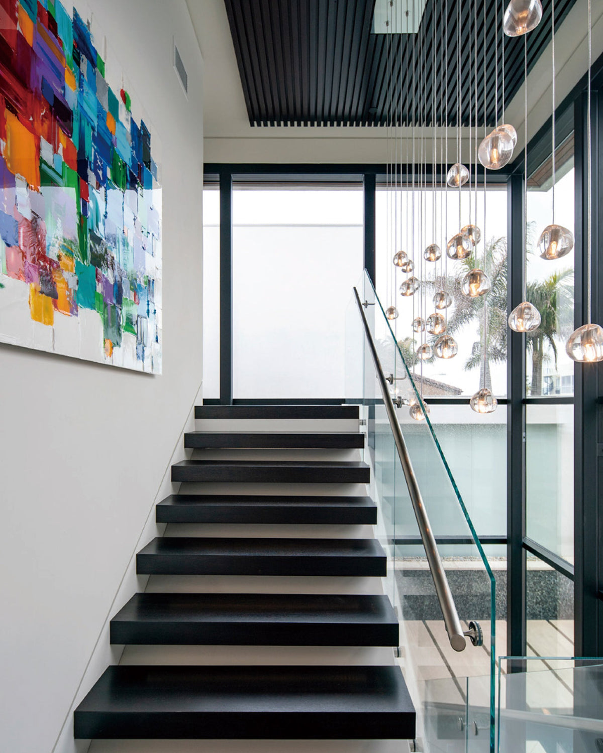 On a bright stair landing with a colourful painting, this Clérachic pendant's amber-tinted heads hang beside a glass balustrade.
