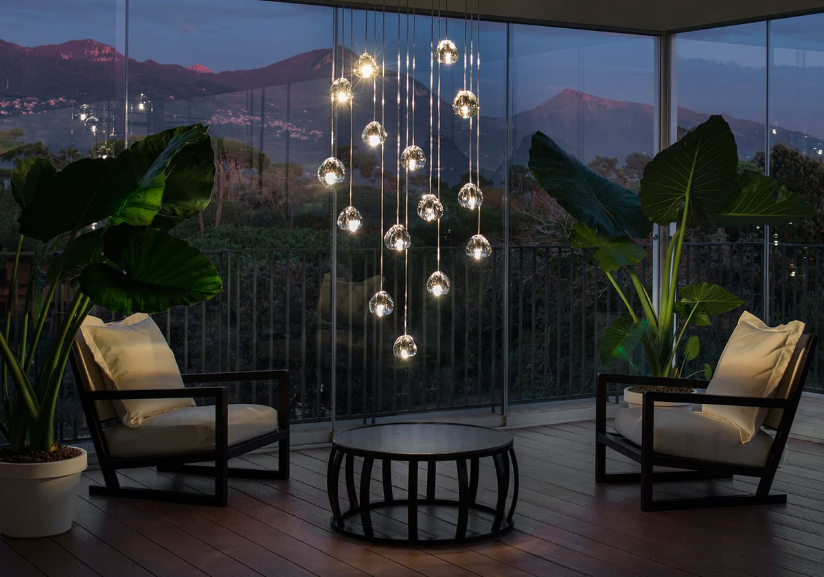 At dusk on a terrace with two armchairs and a round table, this Clérachic pendant hangs as a cluster of clear heads before a mountain view.