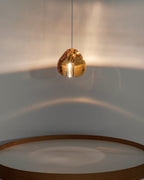 An amber glass head on this Clérachic pendant glows above a rim of warm wood, with a halo of light across the wall.