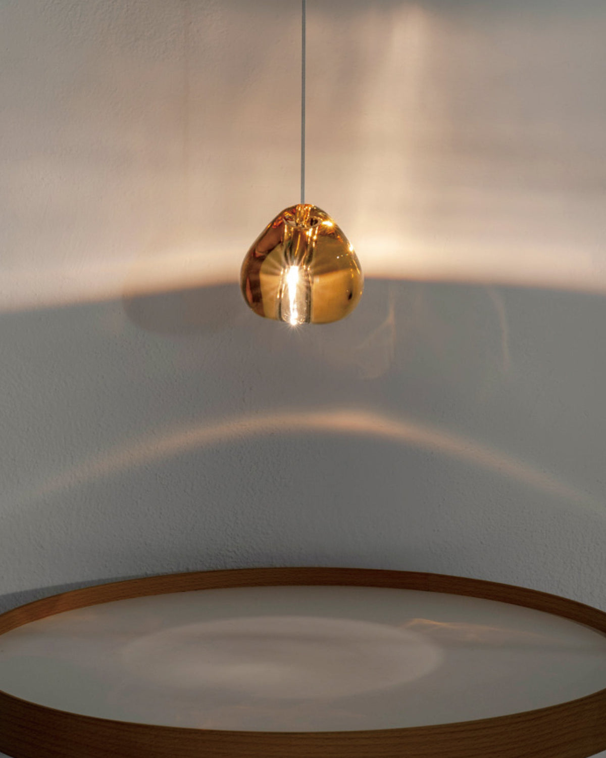 An amber glass head on this Clérachic pendant glows above a rim of warm wood, with a halo of light across the wall.