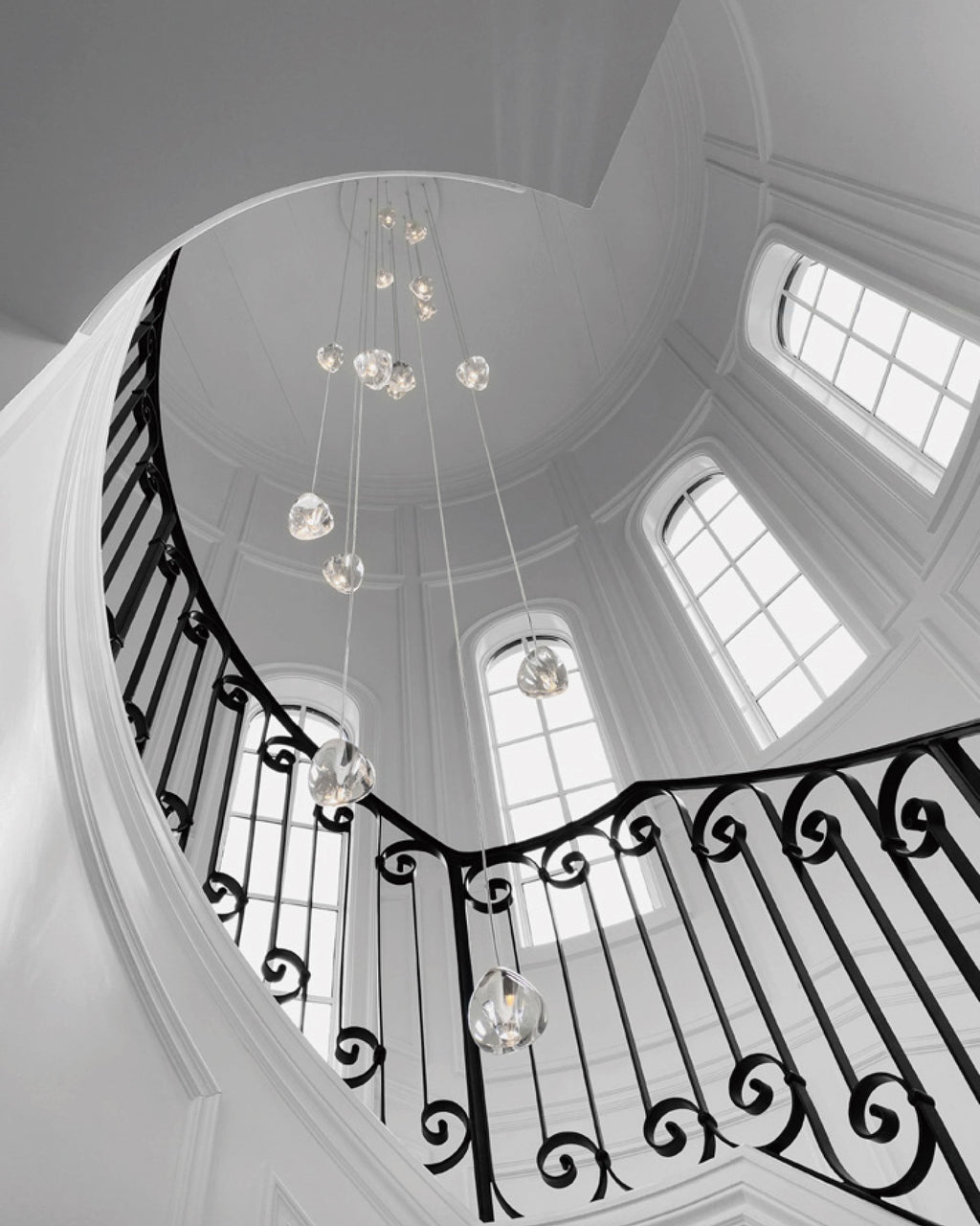 A black-and-white view looking up into a round stairwell with arched windows, with this Clérachic pendant hanging in its centre.