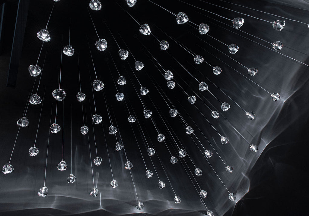 Hundreds of small clear glass heads on this Clérachic pendant hang from fine wires in the dark, with streaks of light below them.