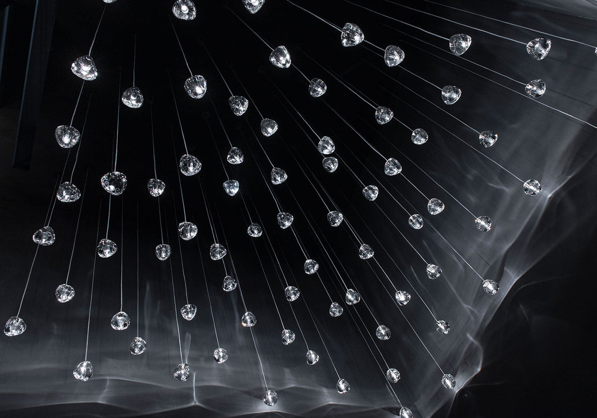 Hundreds of small clear glass heads on this Clérachic pendant hang from fine wires in the dark, with streaks of light below them.