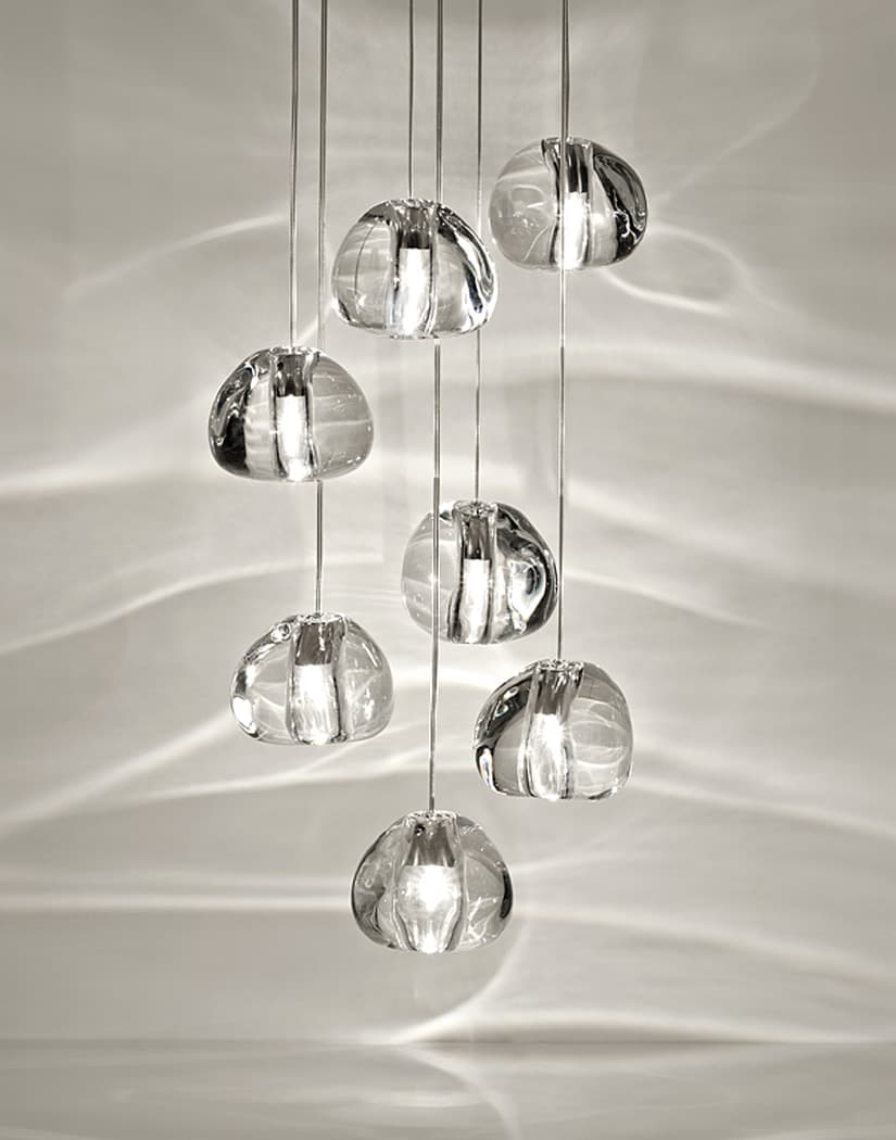 Close view of seven clear glass heads on this Clérachic pendant, with patterns of light across the pale wall behind.