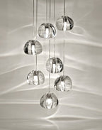 Close view of seven clear glass heads on this Clérachic pendant, with patterns of light across the pale wall behind.