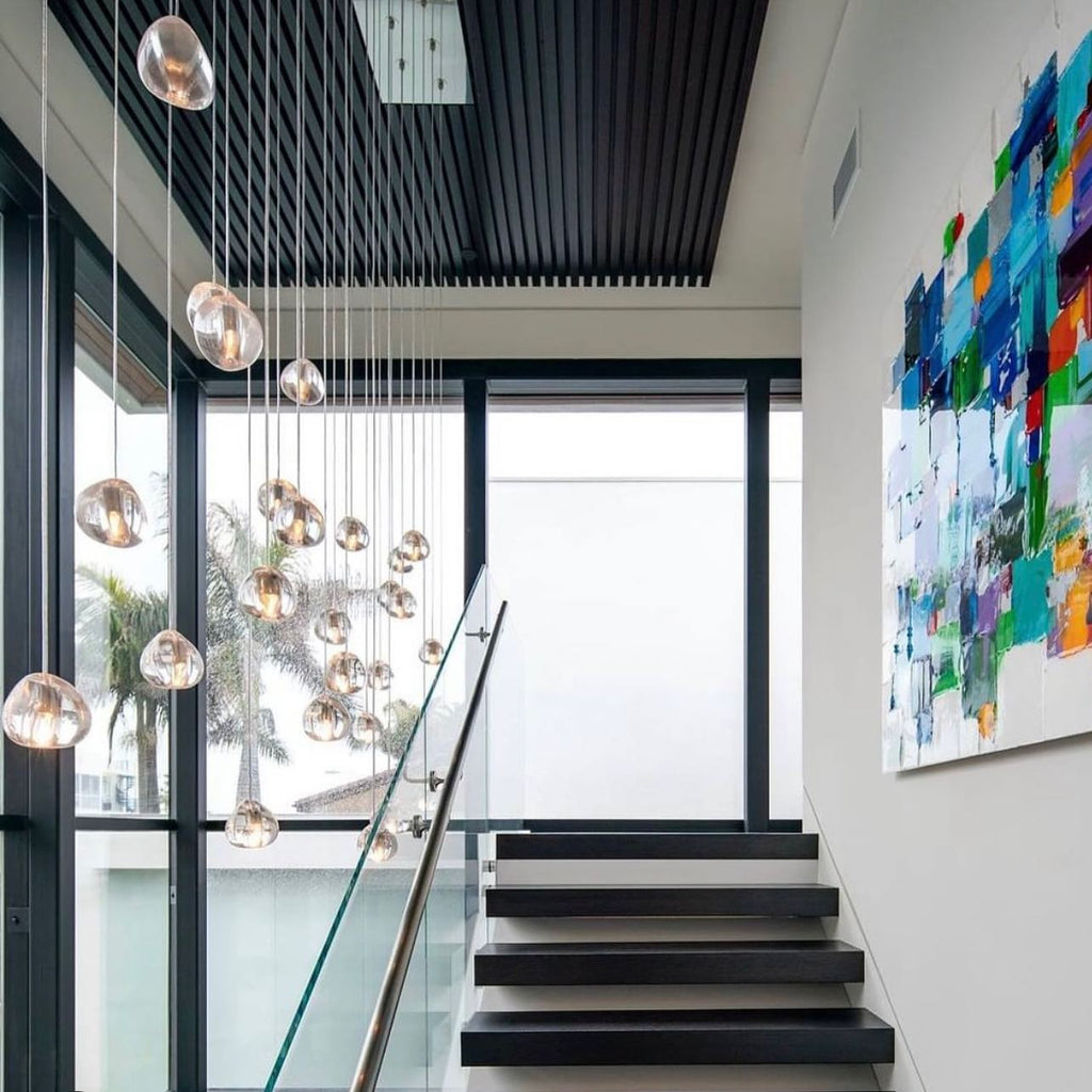 This Clérachic pendant hangs by a stair landing with black treads, a glass balustrade and a bright abstract painting.